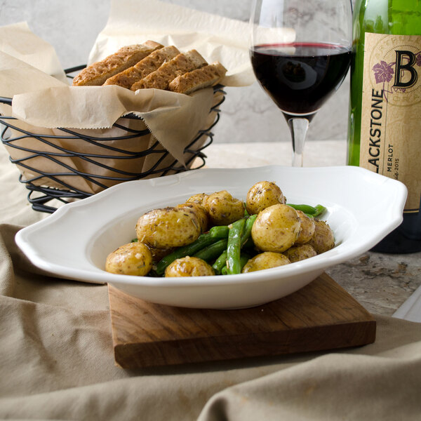 A Villeroy & Boch white porcelain oval deep plate with green beans and potatoes on a table with a glass of wine.