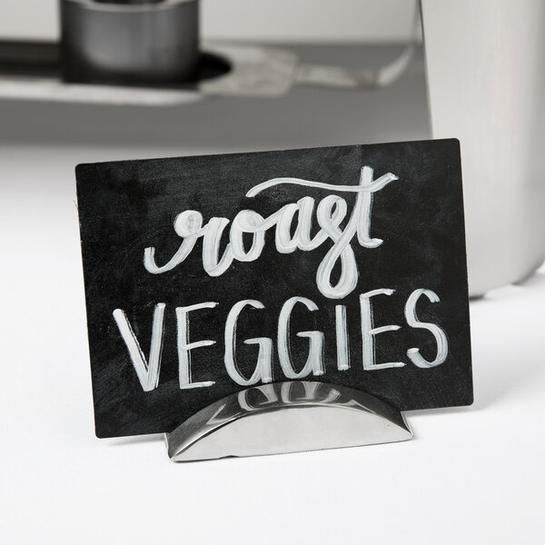 A stainless steel Clipper Mill long single wave table card holder on a counter with a sign in white text.