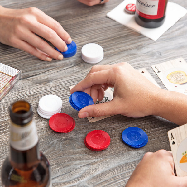 A group of people playing cards with Bicycle white plastic poker chips on a wood table.