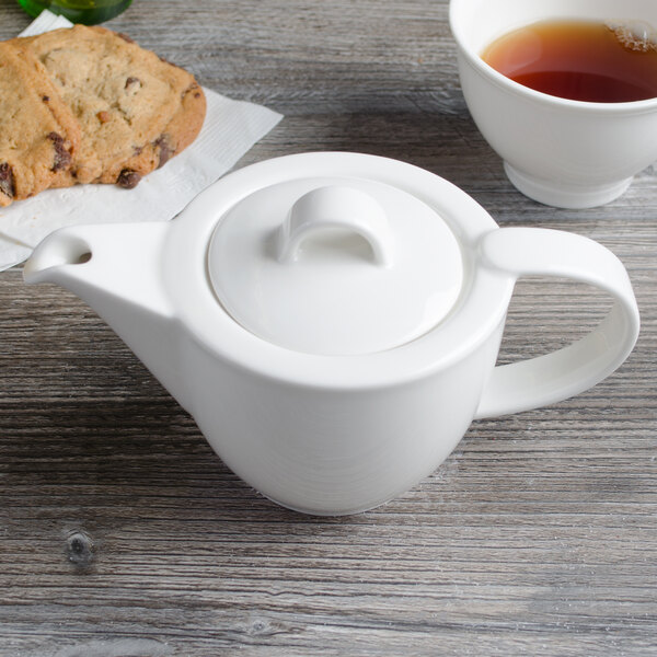 A white Villeroy & Boch porcelain teapot on a wood surface with a cup of tea.