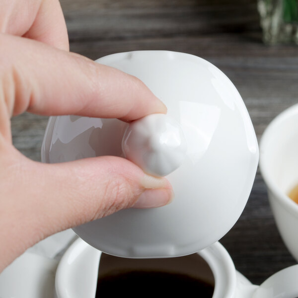 A person's hand placing a white lid on a white Villeroy & Boch coffeepot.