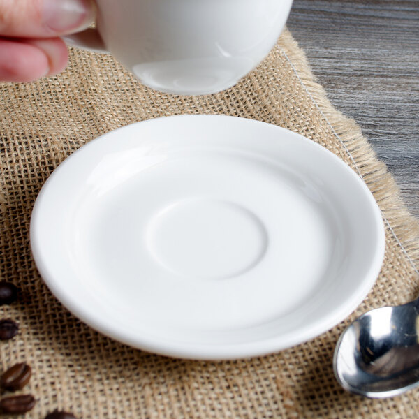 A hand holding a white Villeroy & Boch porcelain cup over a white porcelain saucer.