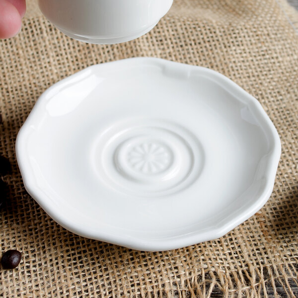 A hand pouring coffee from a white Villeroy & Boch La Scala cup into a white saucer.