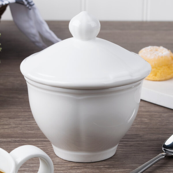 A Villeroy & Boch white porcelain covered sugar bowl with a spoon on a table.