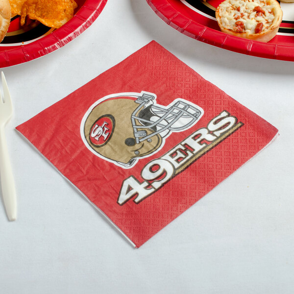 A San Francisco 49ers luncheon napkin with a football helmet on it next to a plate of food.