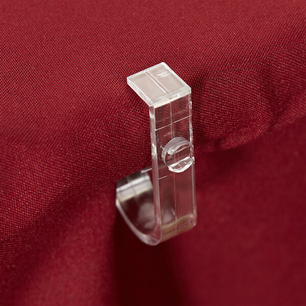 A close-up of a clear Snap Drape "D" Skirt Clip on a red table.