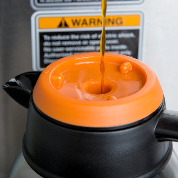 A close-up of a liquid pouring into a black and orange Choice thermal coffee carafe with an orange lid.