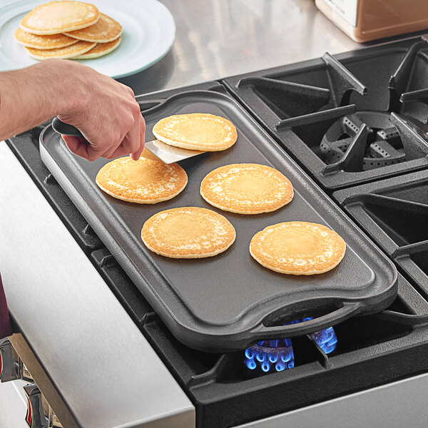 A person using a Choice cast iron griddle to cook pancakes on a stove.