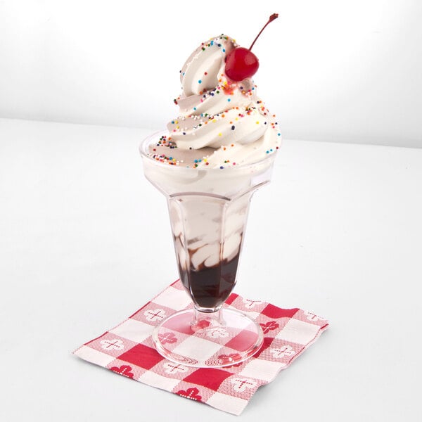 A clear plastic ice cream cup with a sundae and whipped cream and sprinkles on top.