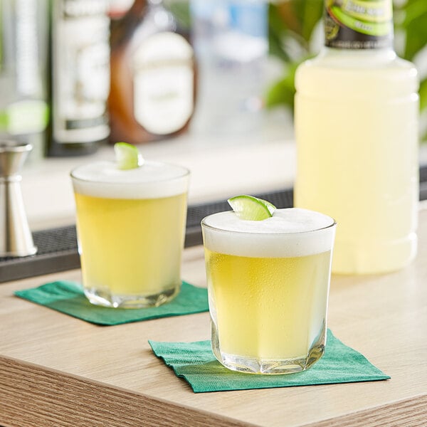 Two glasses of Finest Call lime sour mix on a table.
