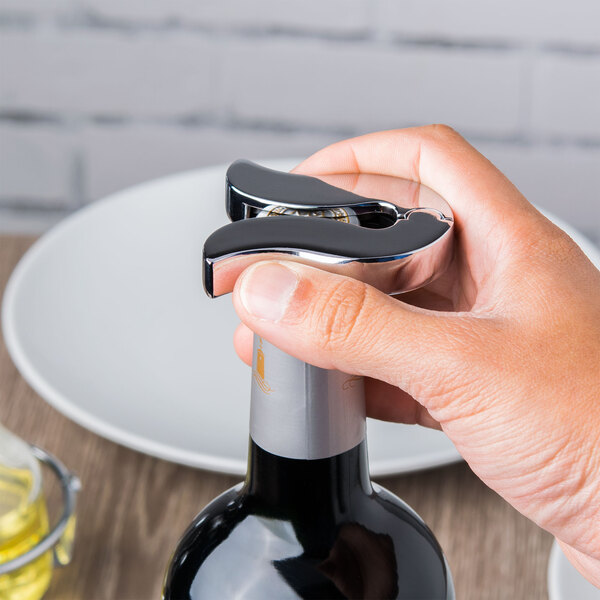 A hand using a Tablecraft Chrome wine bottle foil cutter to open a bottle of wine.