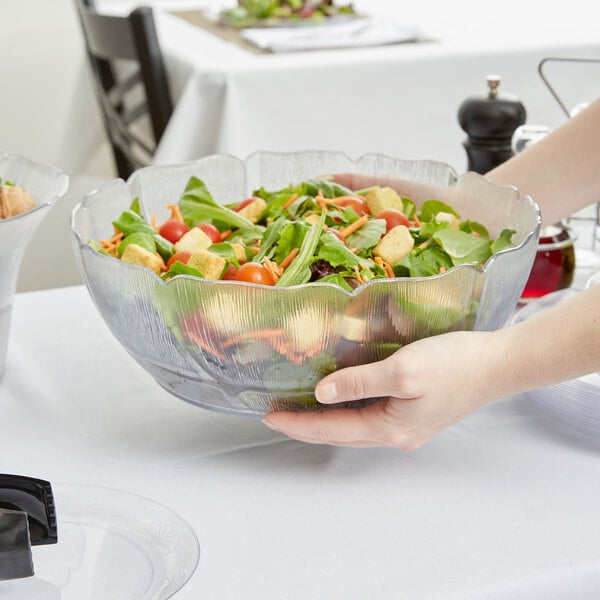 A person holding a Carlisle Petal Mist clear bowl of salad.