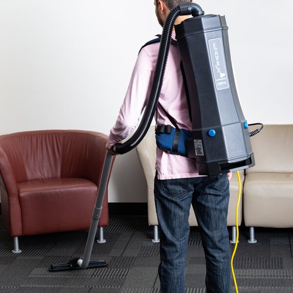 A man using a Lavex backpack vacuum to vacuum a chair.