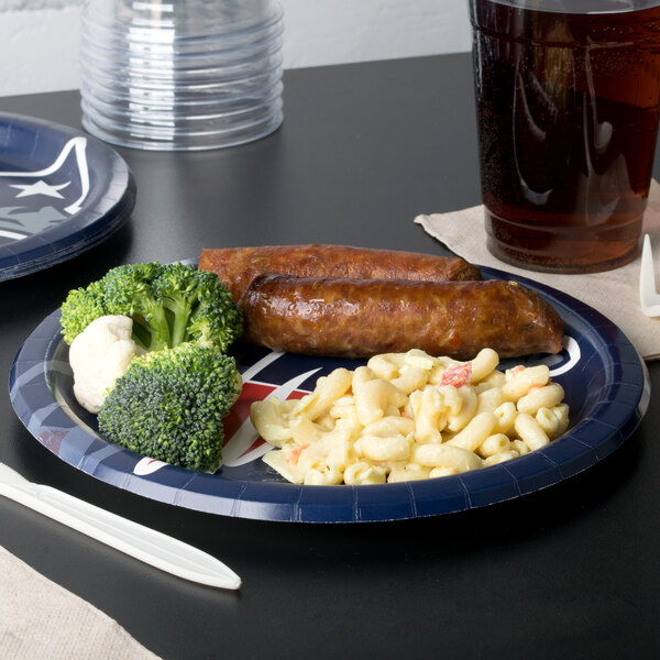 A New England Patriots paper dinner plate with pasta, broccoli, and sausage on it on a table.
