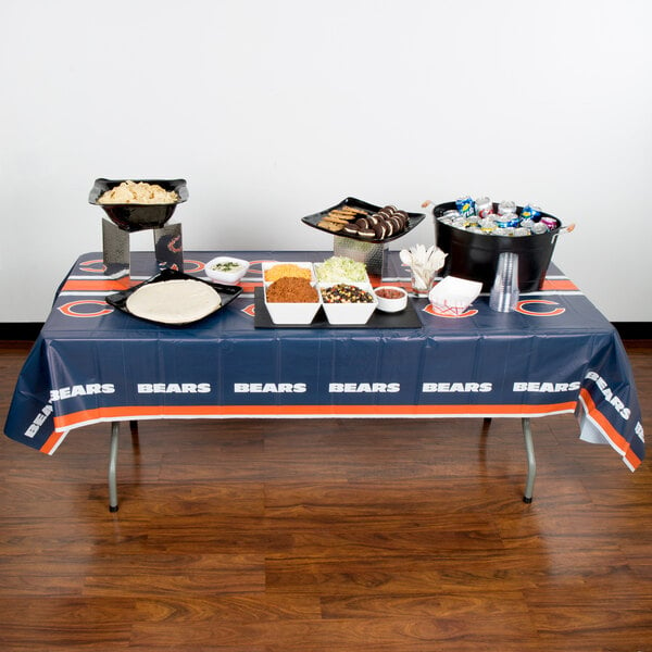 A Chicago Bears plastic table cover on a table with food.