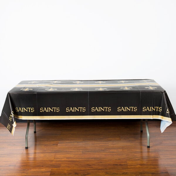 A table with a black tablecloth with gold New Orleans Saints logos on it.