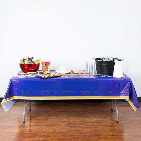 A table with a Creative Converting Baltimore Ravens plastic table cover with food on it.