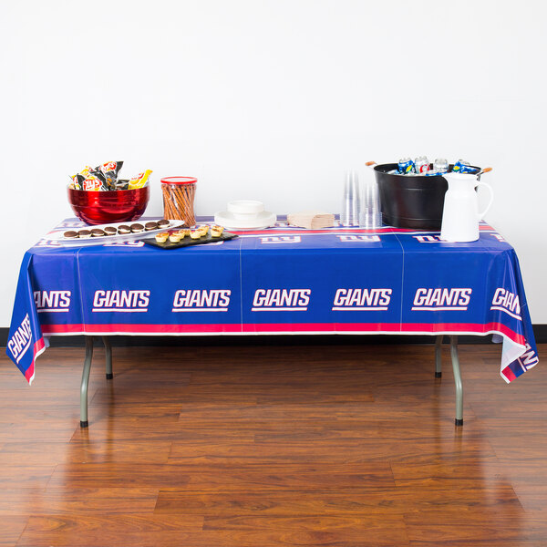 A table with a New York Giants tablecloth and food on it.
