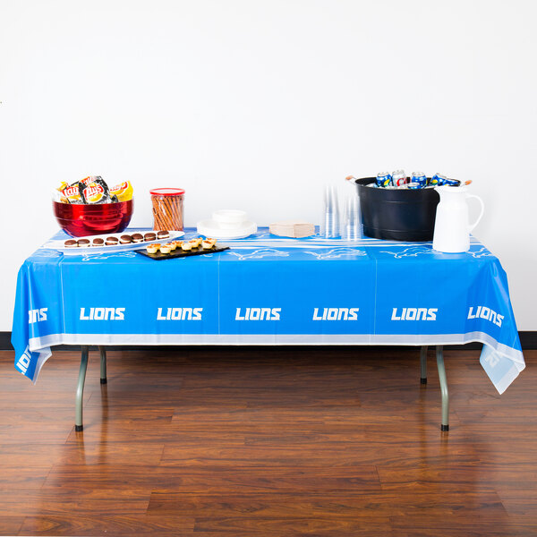A table with a Detroit Lions table cover and bowls of food.