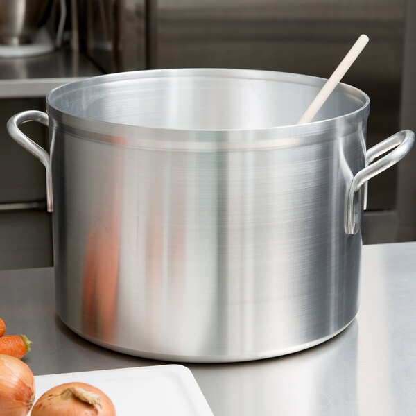 A large silver Vollrath sauce pot with a wooden spoon in it.