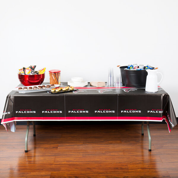 A table with Atlanta Falcons themed food and drinks on it covered with a black and red Creative Converting Atlanta Falcons table cover.