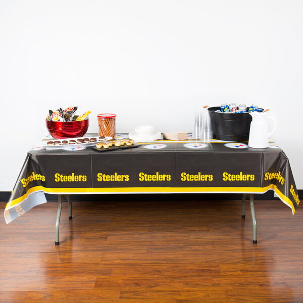 A Pittsburgh Steelers plastic table cover on a table with food.
