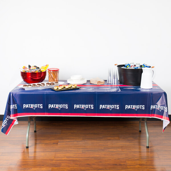 A table with a New England Patriots themed table cover with food on it.