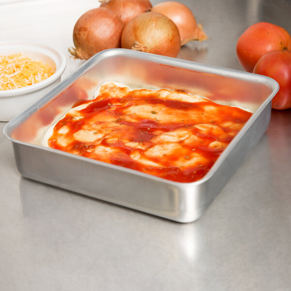 An American Metalcraft square aluminum pan with sauce next to tomatoes and onions.
