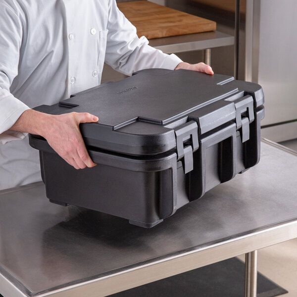 A man in a chef's uniform holding a black container with a black top.