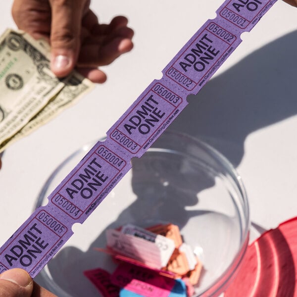 A pair of hands holding Carnival King purple "Admit One" tickets.