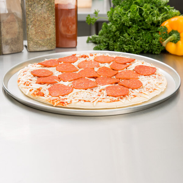 A pizza on an American Metalcraft tin-plated steel pizza pan with pepperoni and cheese.