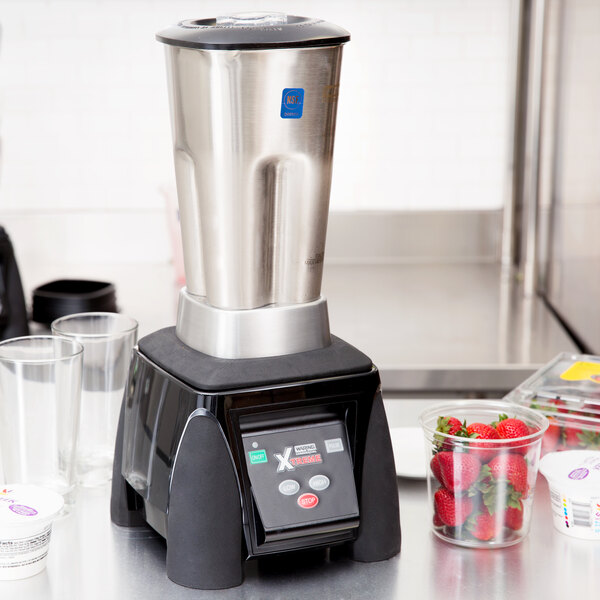 A Waring commercial blender on a counter with a container of strawberries.