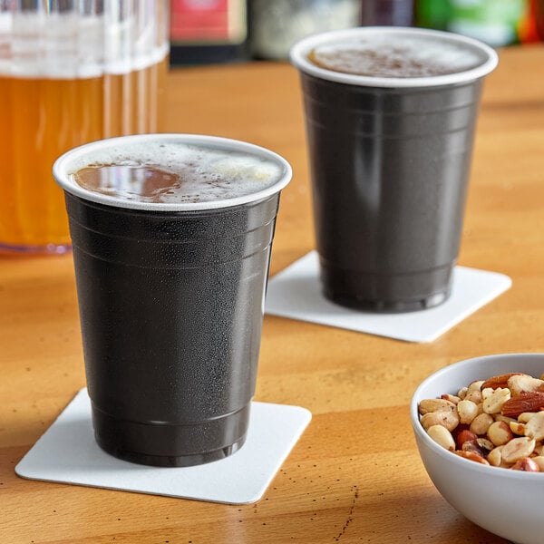 Two black plastic cups of beer on a table with mixed nuts.