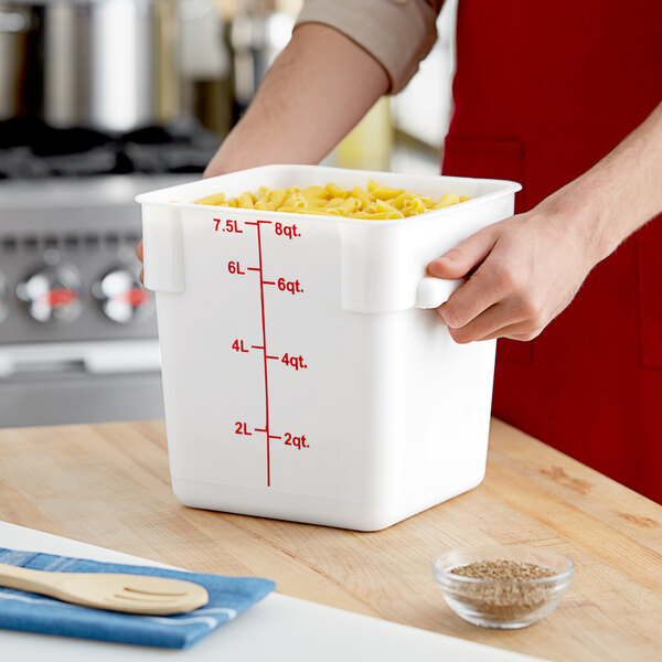 A person holding a white Choice square polypropylene food storage container filled with pasta.
