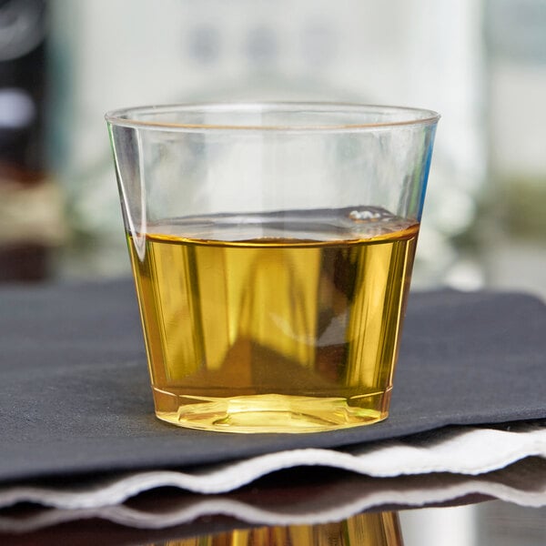 A clear Fineline hard plastic shot cup with a brown liquid inside.