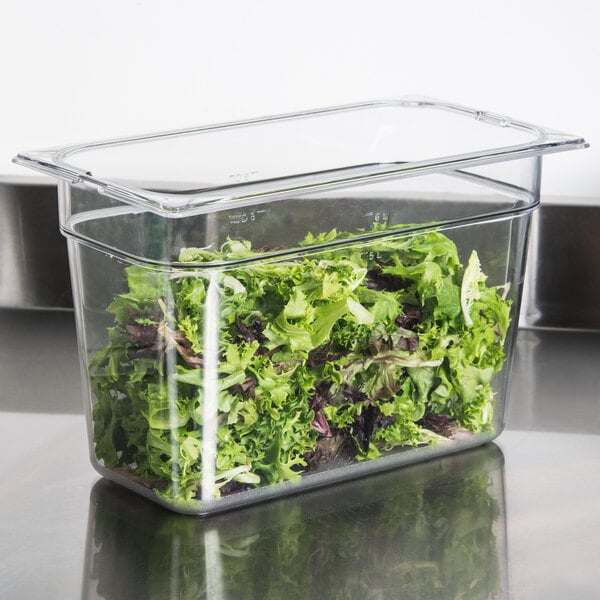 A Carlisle clear polycarbonate food pan filled with lettuce on a counter.