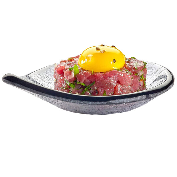 A smoked glass tear drop dish with raw meat and an egg yolk on top.