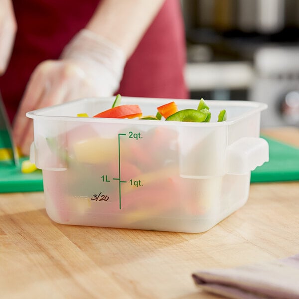 A woman's hand holding a Choice translucent plastic container with vegetables inside.