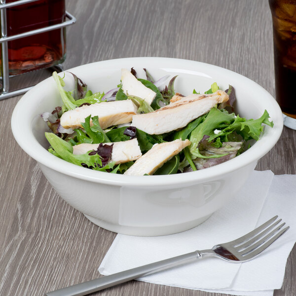 A Tuxton eggshell china footed bowl filled with salad with chicken and lettuce on a white background.