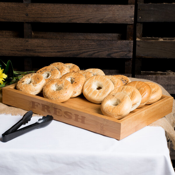 A Rosseto natural bamboo bakery display base with bagels on a table.