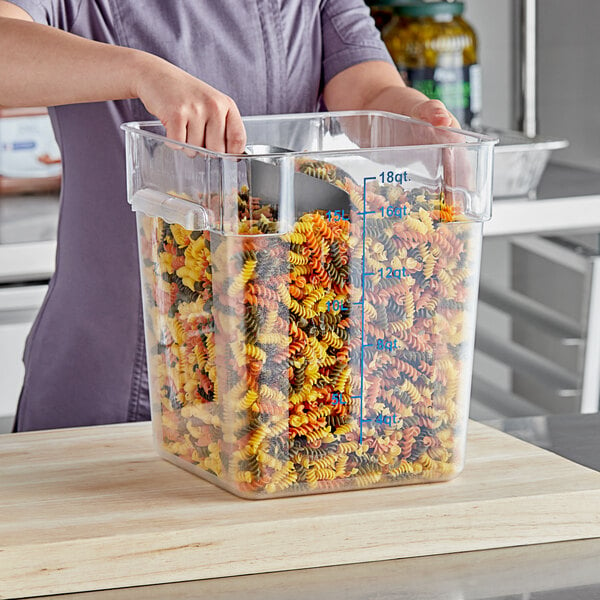 A woman using a Choice clear polycarbonate food storage container to hold spiral pasta on a counter.