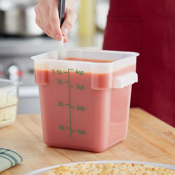 A woman using a spatula to mix liquid in a Choice square translucent food storage container.