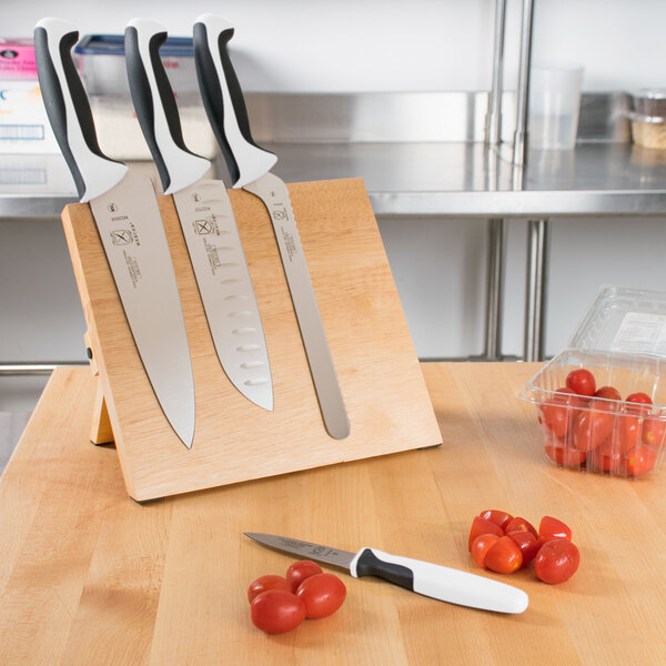 A Mercer Culinary Millennia® knife set on a Mercer Culinary wooden magnetic board with white handles next to tomatoes.