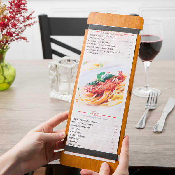 A person using a Menu Solutions Country Oak wood menu board with rubber bands to look at a menu on a table in an Italian restaurant.
