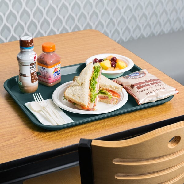 A Choice forest green plastic fast food tray on a table with a sandwich and fruit.