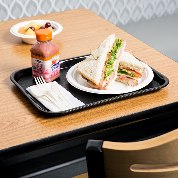 A black plastic fast food tray with a sandwich and a bottle of juice on it.