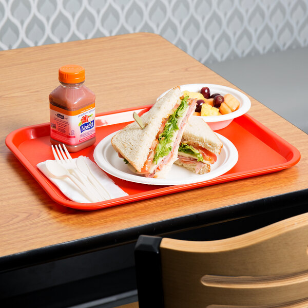 An orange plastic fast food tray with a sandwich and fruit on it.