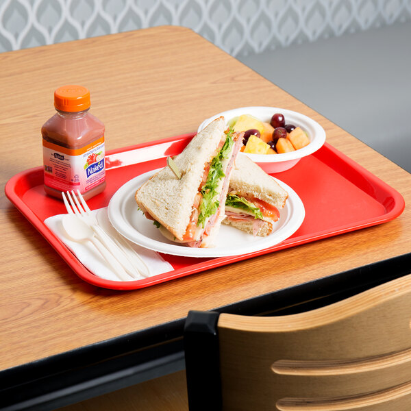 A red Choice plastic fast food tray with a sandwich and fruit on it.