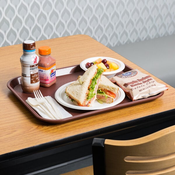 A burgundy plastic fast food tray with a sandwich, fruit, and drinks on it.