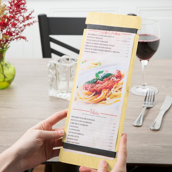 A hand holding a customizable wood menu board with rubber band straps on a table in an Italian restaurant.